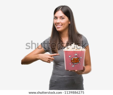 Young beautiful hispanic eating popcorn very happy pointing with hand and finger