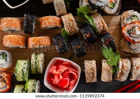 Sushi set food photo. Rolls served on brown wooden and slate plate. Close up view of pickled ginger.