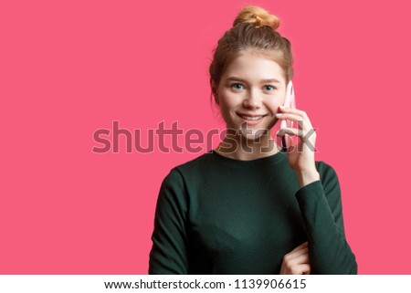 Portrait of young beautiful cute cheerful woman smiling looking at camera while holding smartphone isolated over pink background