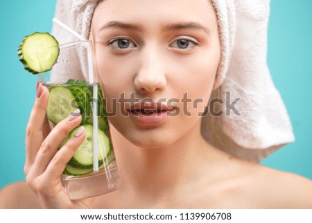 Beautiful caucasian woman with healthy young skin having towel on her head holding a glass of cucumber water as if refreshing herself from the heat of the day. Relaxation SPA concept. Royalty-Free Stock Photo #1139906708