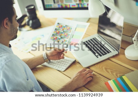 Portrait of young designer sitting at graphic studio in front of laptop and computer while working online