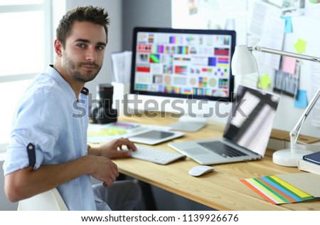 Portrait of young designer sitting at graphic studio in front of laptop and computer while working online