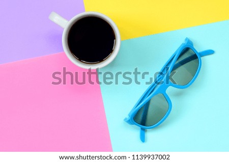 Small white coffee cup and blue sunglasses on texture background of fashion pastel blue, yellow, violet and pink colors paper in minimal concept