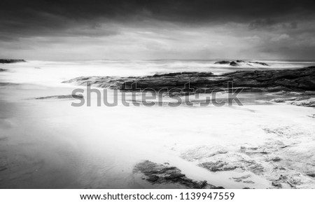 Stormy beach landscape time-lapse with smooth waves and rocks in black and white