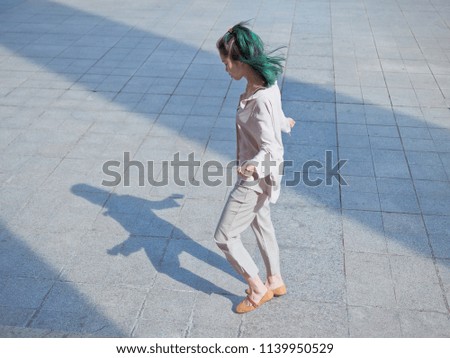 Beautiful young girl with green hair dancing outdoor with black silhouette shadow on ground. Sunny portrait of glamour Chinese stylish lady. Emotions, people, beauty and lifestyle concept.