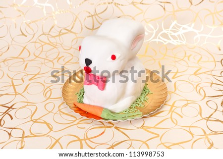 White rabbit cake with marzipan carrot on golden plate and background