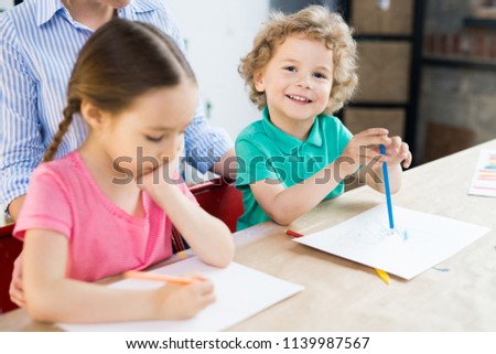 Smiling cute little boy drawing with color pencil together with girl at the table