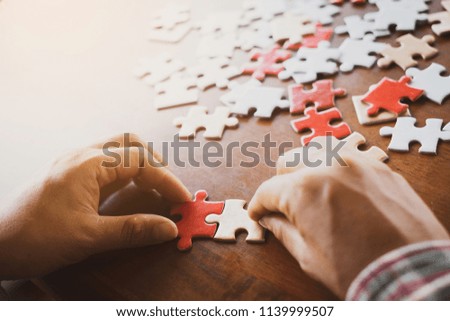 Hand holding piece of blank jigsaw puzzle on wooden background.