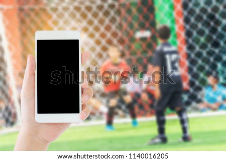 woman use mobile phone and blurred image of asian boys soccer game in front of the goal   