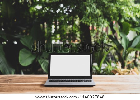 Laptop computer with blank white screen on empty workspace wooden desk and blurred green trees bokeh background, Working everywhere concept