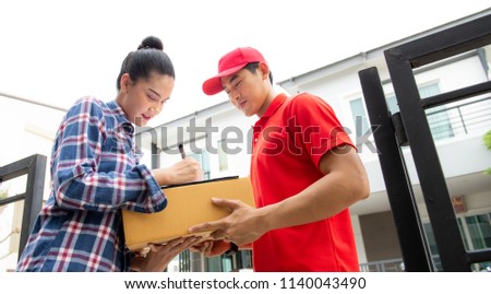 
Young woman signing while receiving courier from delivery man at home,
Young delivery man holding a cardboard box while beautiful young woman putting signature in clipboard,Signing to get her package
