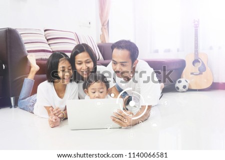  Happy asian family and little daughter are lying on a floor at home and working with laptop computer with virtual icon diagram