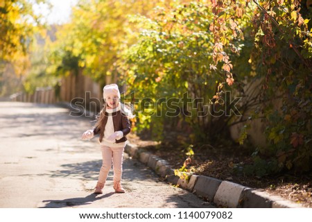 Autumn children's fashion. A little girl dances, jumps and rejoices in the fall against a background of yellow and red foliage on trees and bushes. Joy and happiness