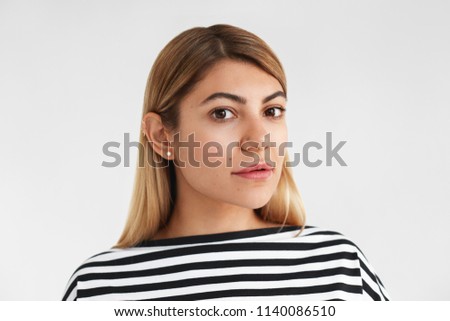 Close up portrait of attractive fashionable young Caucasian female with beautiful features, blonde loose hair and rosy cheeks looking at camera with subtle smile. People and natural beauty concept