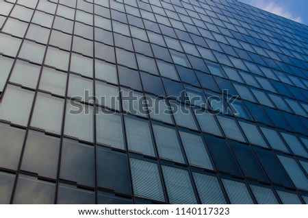 Bottom view glass grey square Windows of modern city business building skyscraper and blue sky with white clouds. Receding perspective, movement forward and up.

