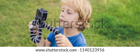 Little boy shoots a video on an action camera against a background of green grass. BANNER long format