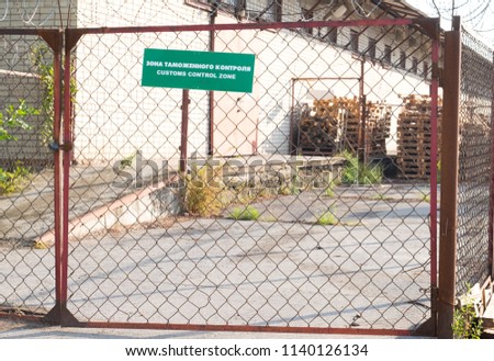 Grid fence with green sign "customs control zone" in English and Russian languages