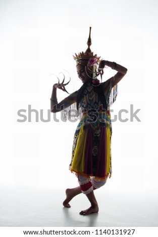 The lady in Southern thai classical dancing suit is posing by raise hands up,bend knees down and cross legs,traditional dancing pattern,silhouette style