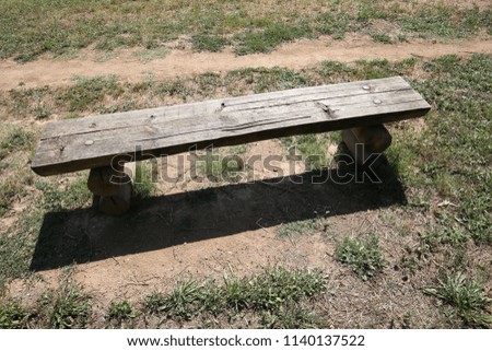 Outdoor view of an isolated wooden bench located in a french public park in France. Pathway in front of the seat with dry grass. Object shadow on the brown ground. Nobody in the garden.