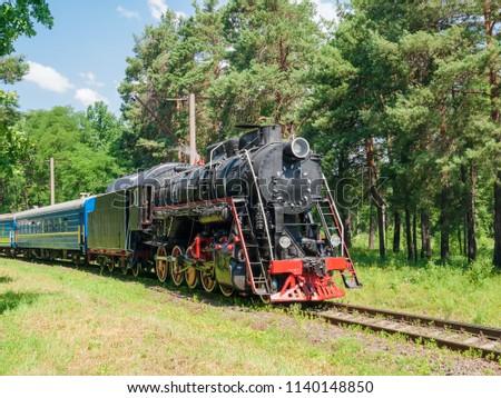 Moving passenger train with old steam locomotive on a section of the railroad located in forest
