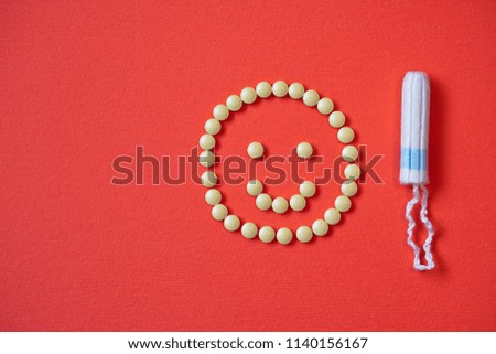 Background red on the theme of a monthly menstrual cycle. Smile PMS and protection against it. Tampon and analgesic tablets. Intimate topic of feminine hygiene. Stock photos