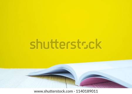 Opened book on white table with yellow wall background.