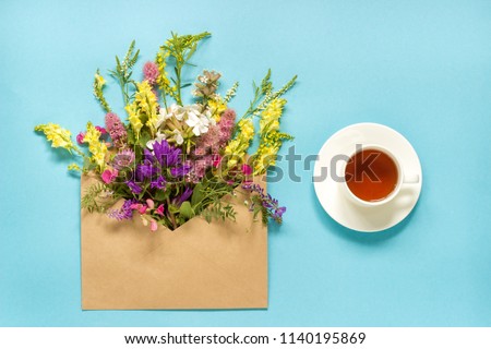 Field colorful rustic vintage flowers in craft envelope and cup of  herbs tea on blue turquoise background Concept Good morning  Summer Teatime Tea party Greeting card Flat Lay Copy space