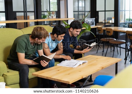 Three fellow students studying and preparing for exam. Young men sitting on couch in library reading room. Education concept.