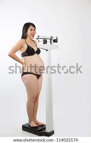 Pregnant Asian woman standing on a medical scale wearing panties and bra.