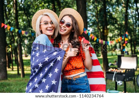 portrait of happy women in hats and sunglasses with american flag in park