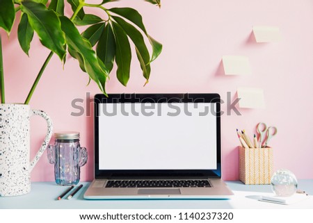 Stylish and creative desk with laptop mock up screen, tropical leaf, office accessories and memo stick. Pink background wall. Design home office interior. 
