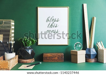 Green modern and stylish room with gold mock up poster frame, office accesories, boxes and design plants. Creative composition of desk in green interior.