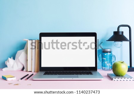 Stylish and creative desk with laptop mock up screen, books, cat figures, office accessories and lamp. Blue background wall. Design home office interior. 