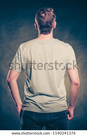 Back rear view of fashionable man in blank shirt with empty copy space. Guy in studio on black. Casual fashion advertisement. Instagram cross filter.