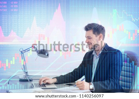 Double exposure of graphs and financial trader working with laptop at table in office. Forex concept