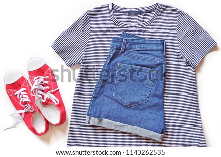 Summer trendy women's outfit. Striped t-shirt, blue shorts and red gumshoes on a white background. Flat lay photography, top view clothes combination. Image for fashion blog