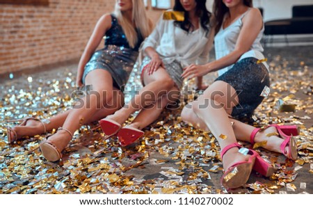 Let the party begin! Cropped image of three attractive young women having fun together. Sitting on the floor with confetti falling. Celebrating holiday in big company of close friends.