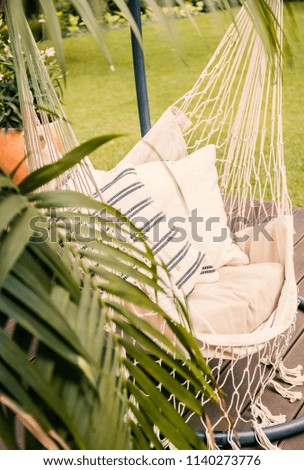 Close-up of a boho hammock hanging in a sunny garden with a palm tree and green lawn