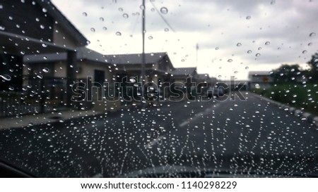 A very rare rainy day with car and people as seen through car windows with rain drops visible on the window. Blured background with rains drop on glass and cars on the road.- soft focus
