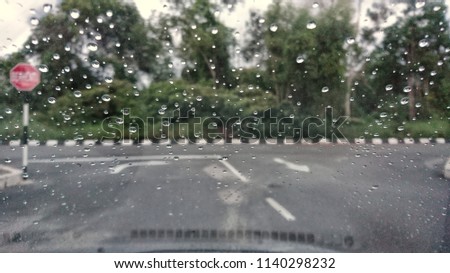 A very rare rainy day with car and people as seen through car windows with rain drops visible on the window. Blured background with rains drop on glass and cars on the road.- soft focus