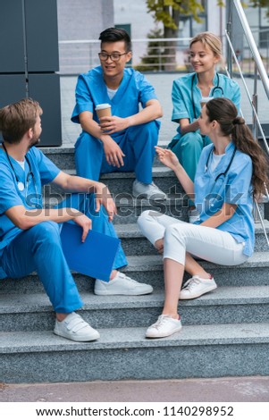 smiling multicultural medical students talking while sitting on stairs