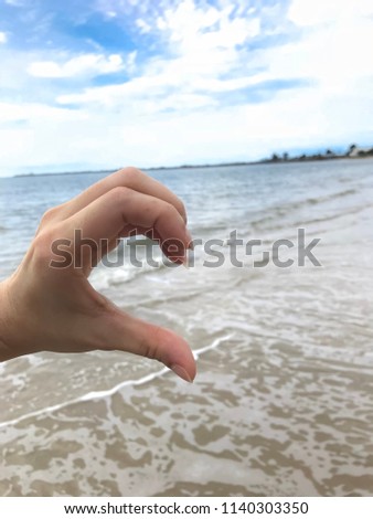 one hand show half of heart to have area for other hand someone with sand and sea background - miss you concept