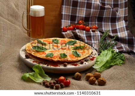 pizza thin with tomato, cheese, special, on a wooden stand close-up with beer in a glass mug.