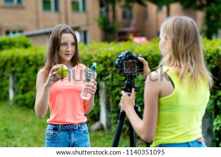 For girl schoolgirls, summer in nature. Records a video about healthy eating. In his hands holds a green apple and a bottle of water. Record video lesson for Internet. Use camera with tripod.