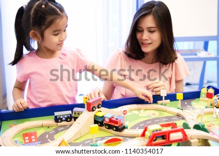 Mother and daughter are spending time together. They are playing colorful wooden toys on table. Mother teaches her daughter how to play. Pure love between mother and child concept.              