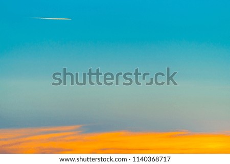 Sunrise landscape with airplane flying across blue sky and leave trail in clear sky above long orange cloudy line. Dawny cloudscape with copy space.