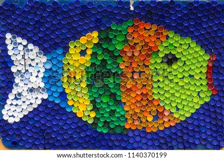 Fish mosaic decoration made of colorful plastic bottle caps . Summer season and travel concept. Handmade crafts. Recycling art. Royalty-Free Stock Photo #1140370199