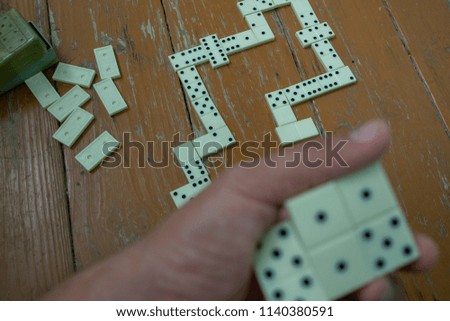 Domino knuckles laid out on a wooden table for playing and out of focus in the foreground a player's hand holding a few dominoes