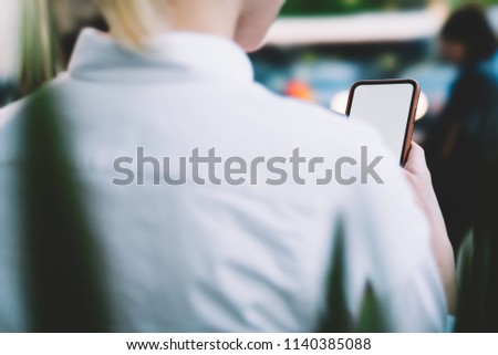 Cropped back view of young woman holding smartphone with blank screen area for internet advertisement.Hipster female blogger updating app on mobile phone with mock up area using 4G connection