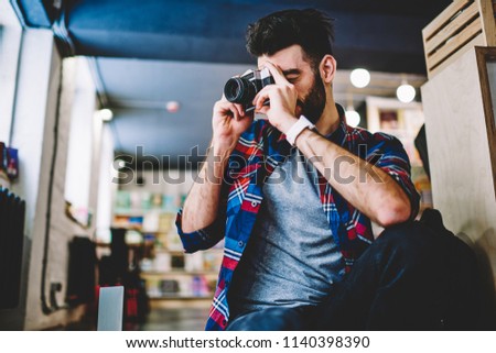 Young handsome male amateur photographer making pictures using vintage camera at university campus, caucasian hipster guy casual dressed taking photo with favourite retro technology indoors